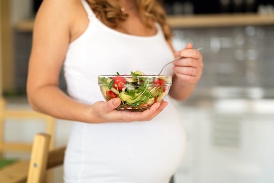 Pregnant woman on healthy diet holding salad